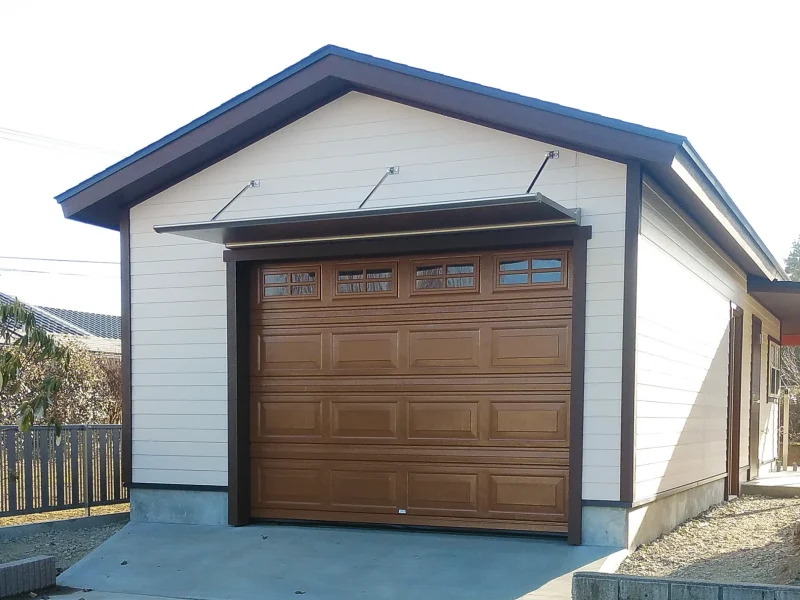 施工例 渋く塗装されたオーバードアとL字の差掛け屋根が特徴的なガレージ